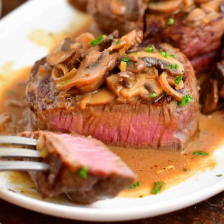 sliced steak Diane on a white plate with a piece of a fork.