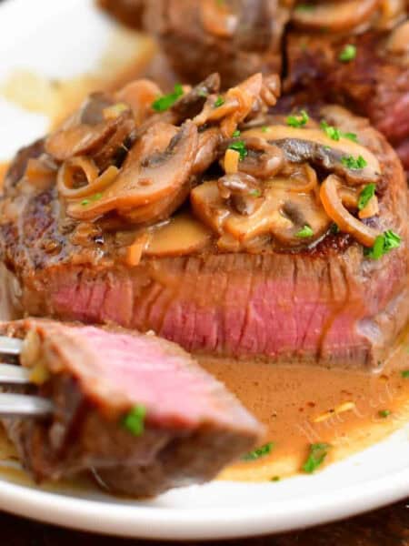 sliced steak Diane on a white plate with a piece of a fork.