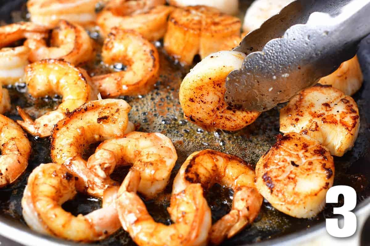 flipping scallop in the skillet next to shrimp and scallops.