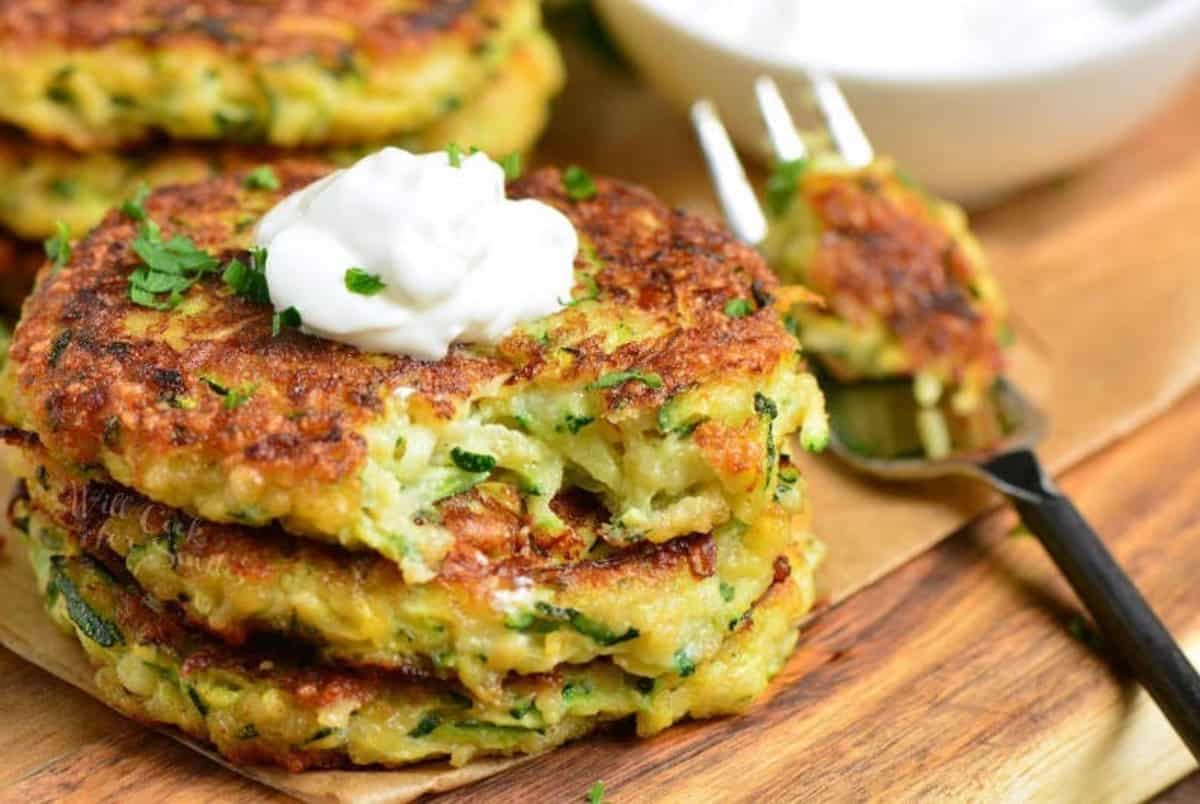three zucchini fritters stacked and topped with sour cream with a fork.