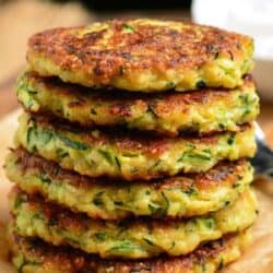 six zucchini fritters stacked on top of each other on parchment paper.