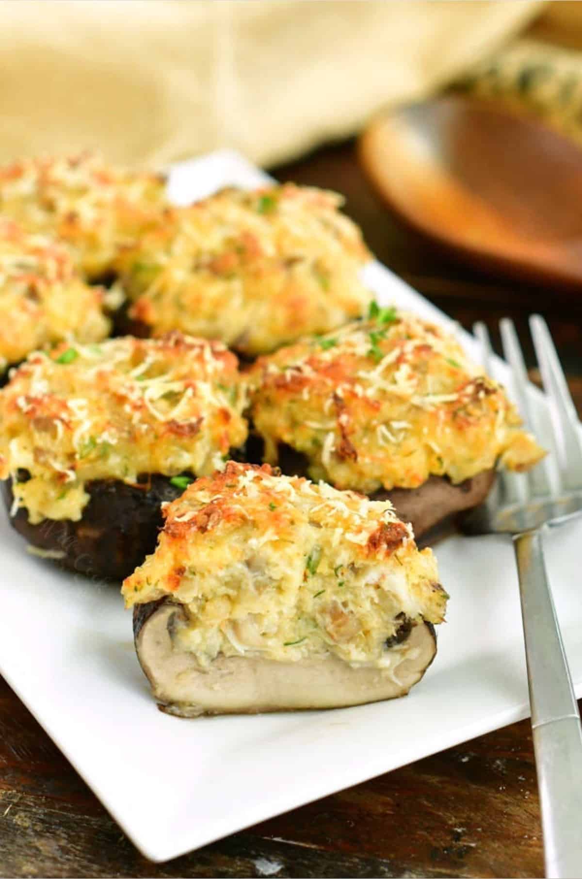 stuffed mushrooms on a white plate and first mushroom cut in half with a fork next to it.