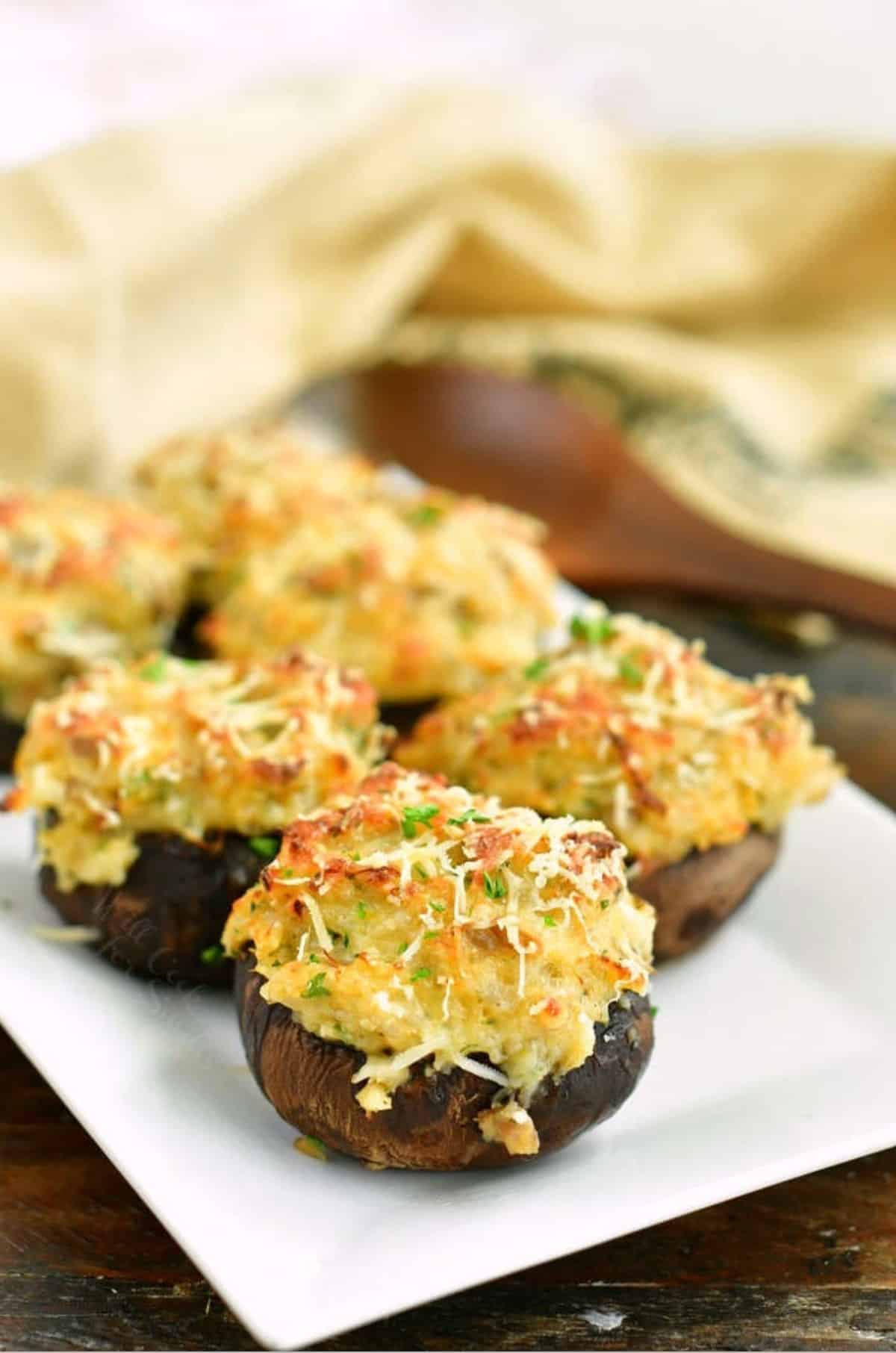 several stuffed mushrooms on a white plate with wooden spoon on the background an burlap towel.