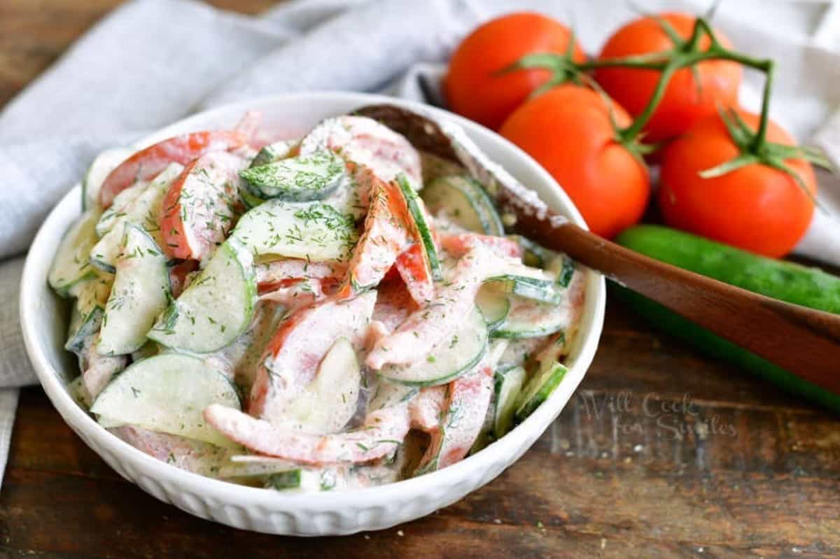 cucumber tomato salad in a white bowl with a wooden spoon with tomatoes and cucumber.