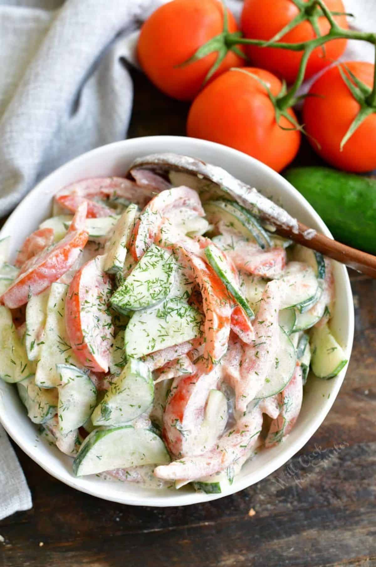 tomato cucumber salad mixed in a white bowl next to tomatoes on a vine.