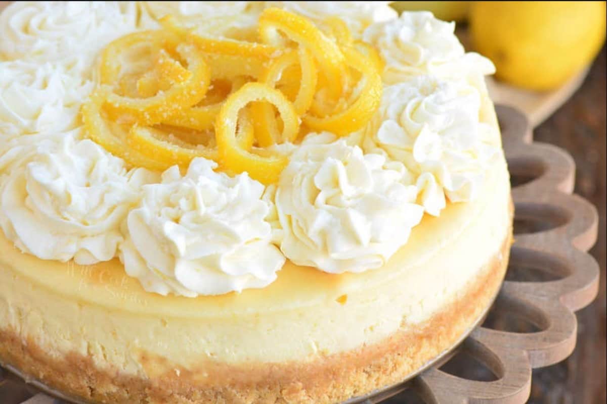 whole lemon cheesecake with frosting and lemon peels on cake stand.