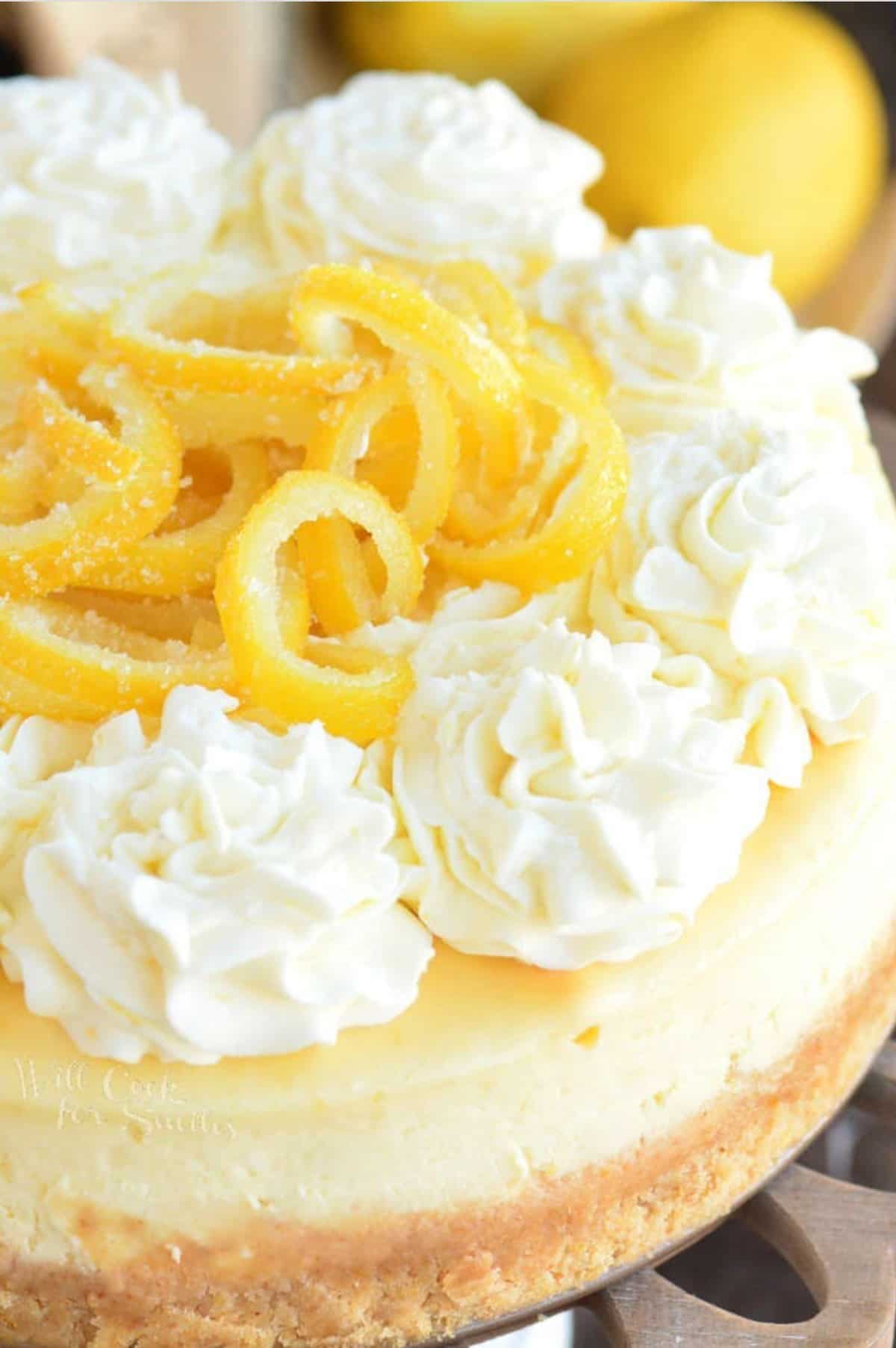 candied lemon peels and frosting top a lemon cheesecake.