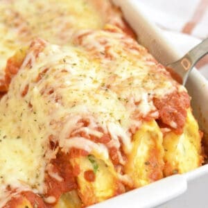 pulling out some manicotti from the white baking dish with a silver spatula.