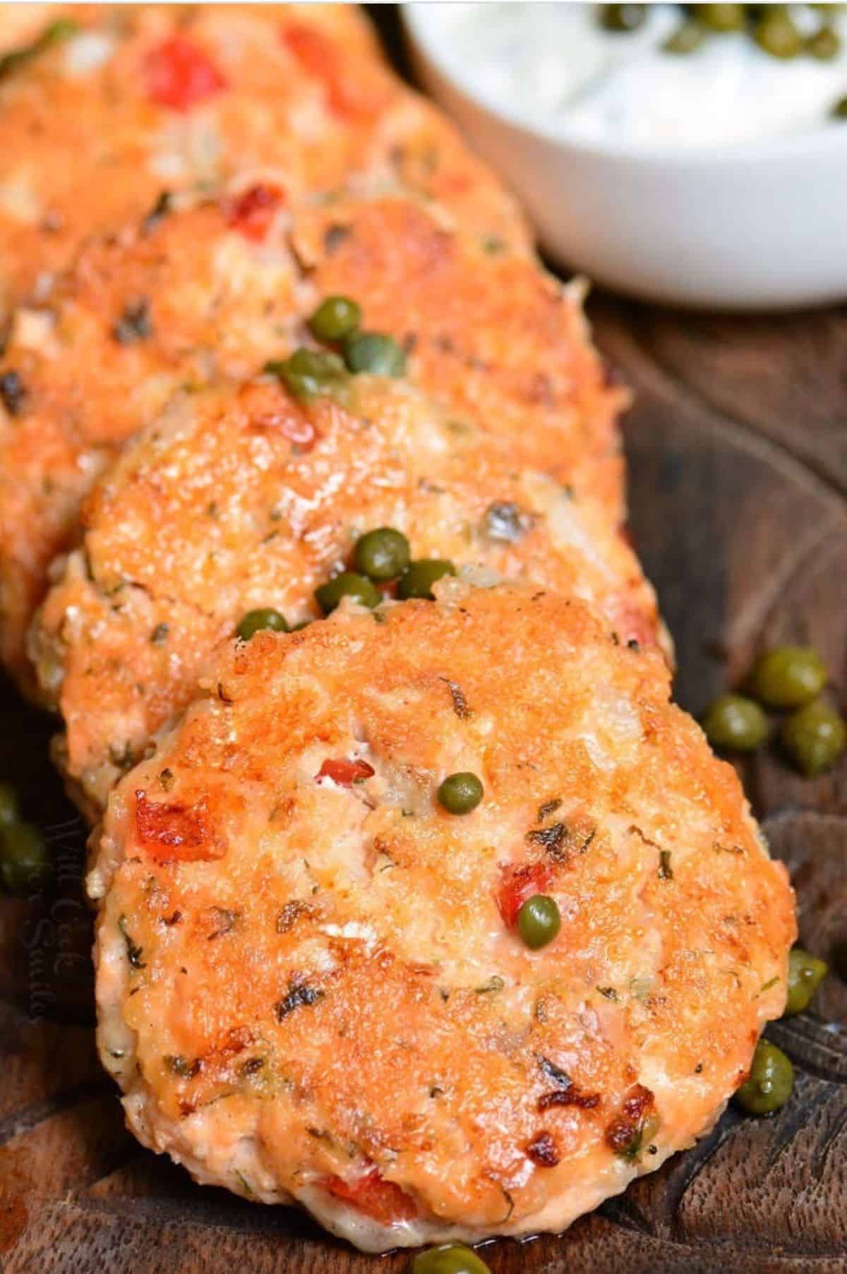 several salmon patties side by side on wooden plate with capers.