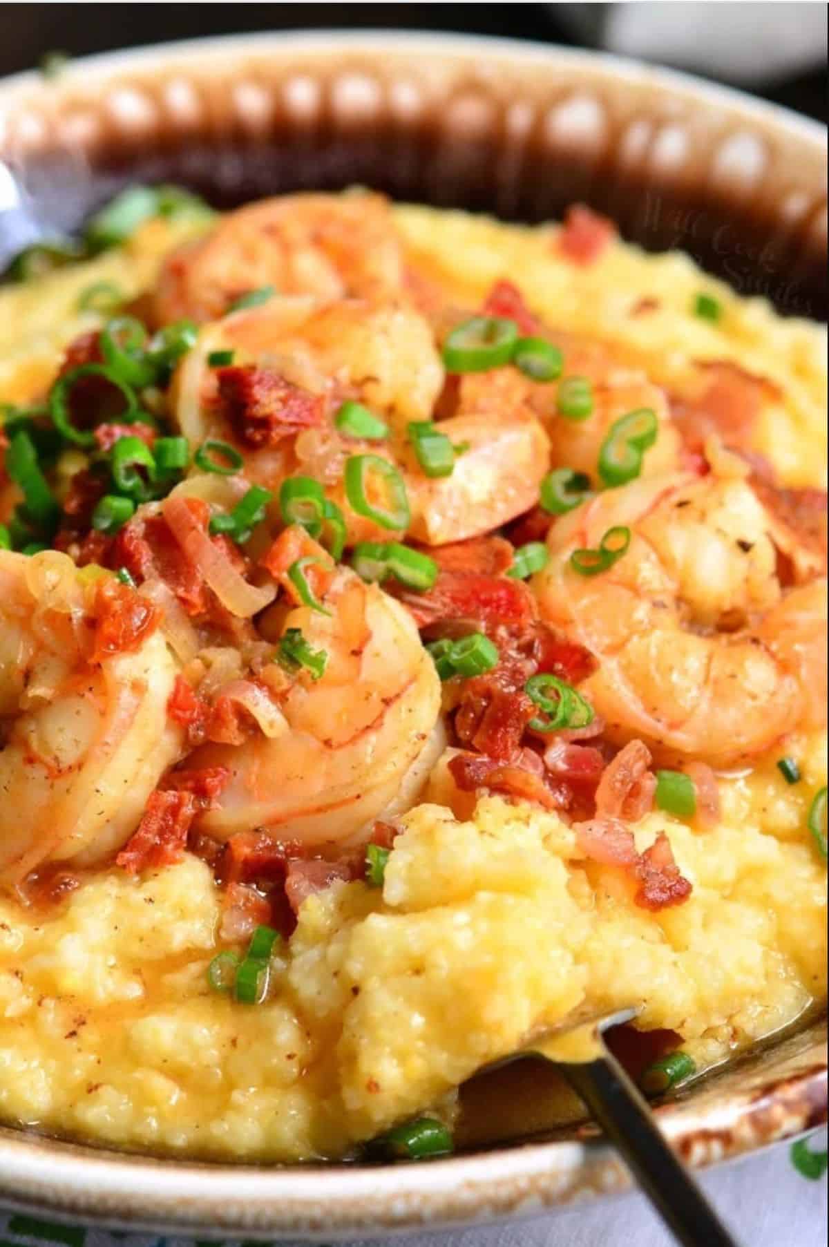 scooping out some cheesy grits from the bowl of shrimp topped over grits.