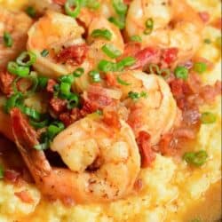 several large shrimp, tomatoes, and green onions with sauce over the grits.