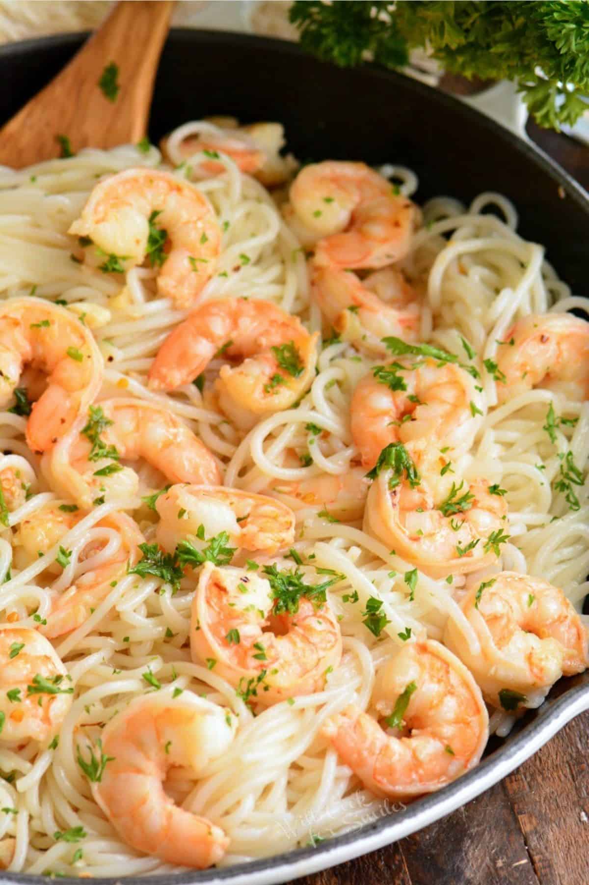 shrimp scampi and spaghetti in a white skillet with a spoon.