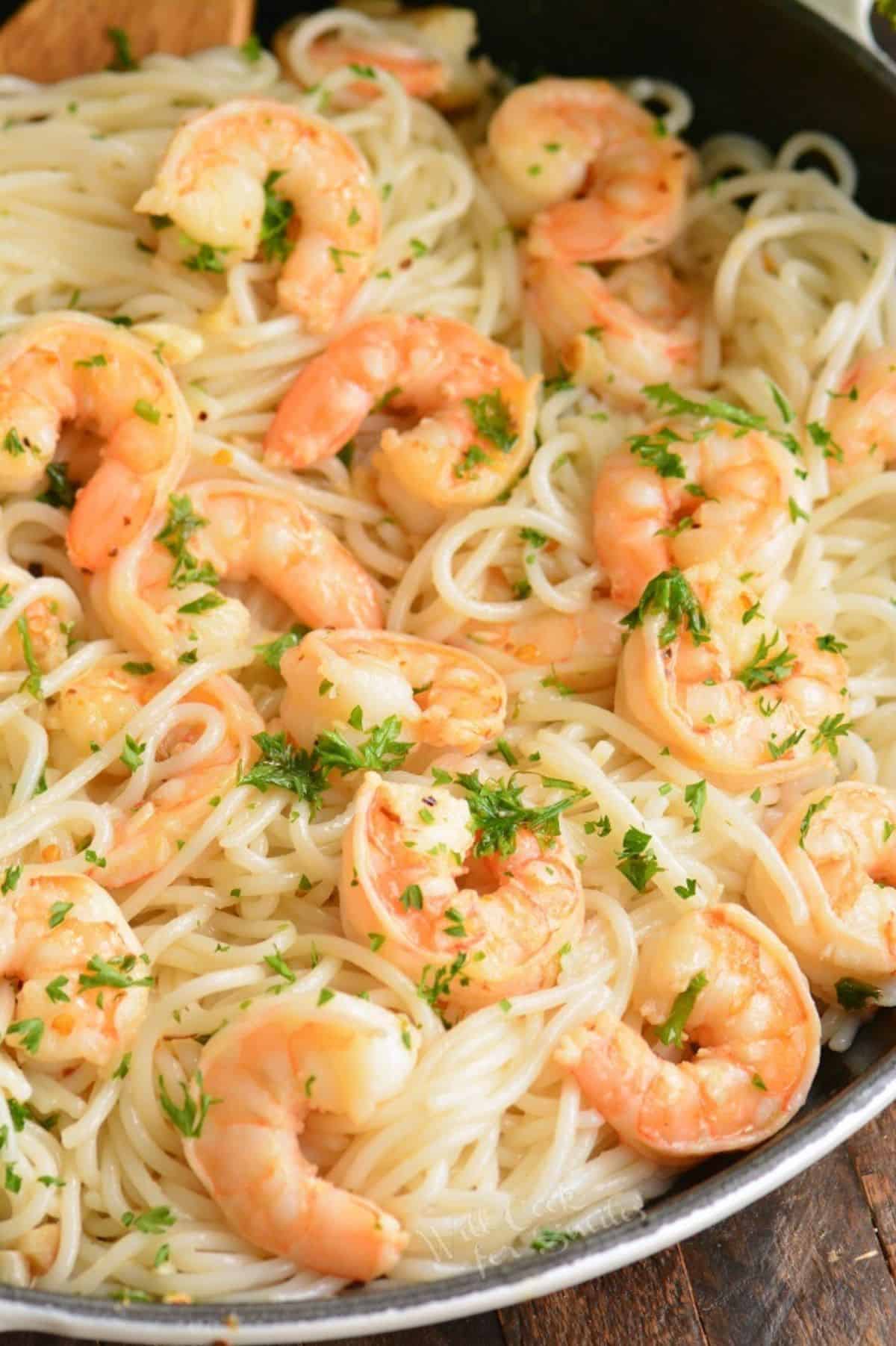 shrimp scampi over spaghettini in a skillet topped with some parsley.
