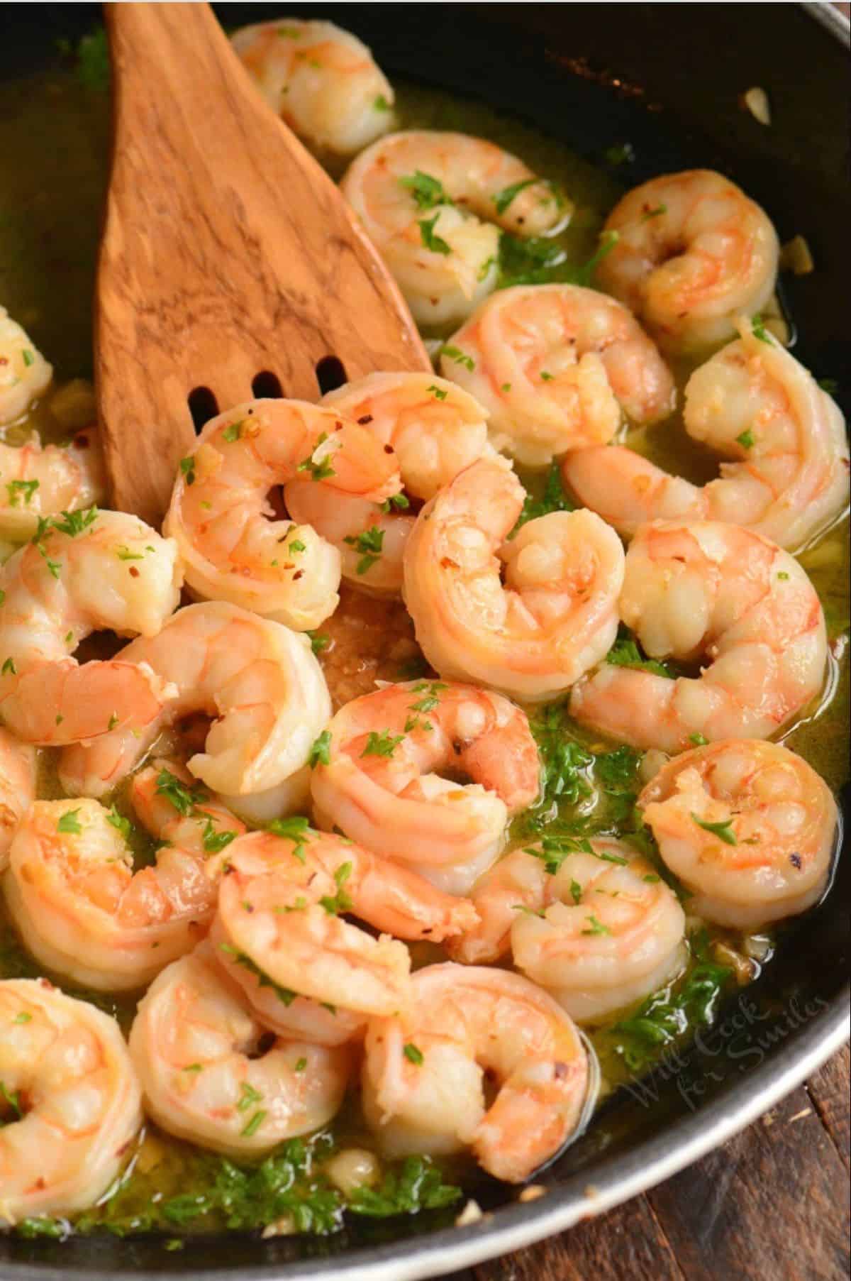 shrimp scampi in sauce in the skillet with a wooden spoon.