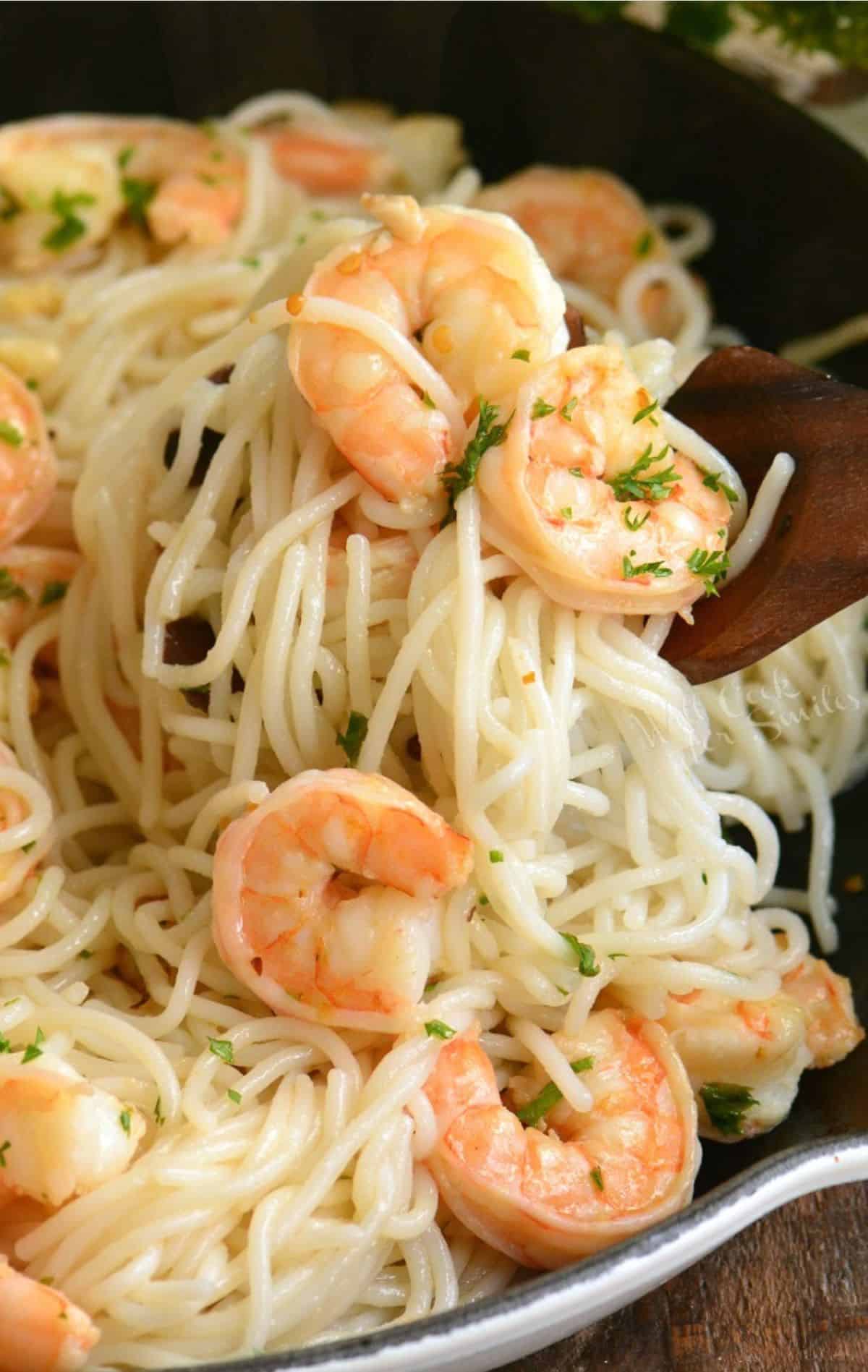 scooping out some shrimp scampi and pasta from the skillet with wooden spoon.