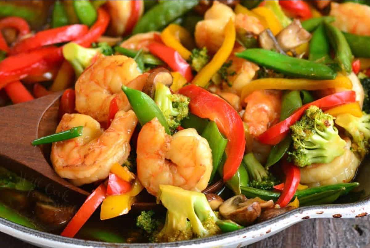 spooning some shrimp stir fry with lots of veggie from the skillet.