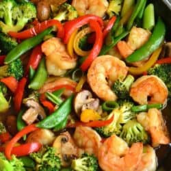 shrimp and lots of vegetables in sauce in a skillet with a wooden spoon.