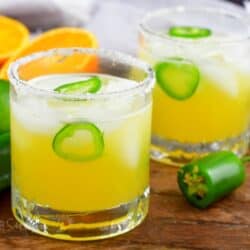 two short glasses with yellow spicy margarita with jalapeno slices.