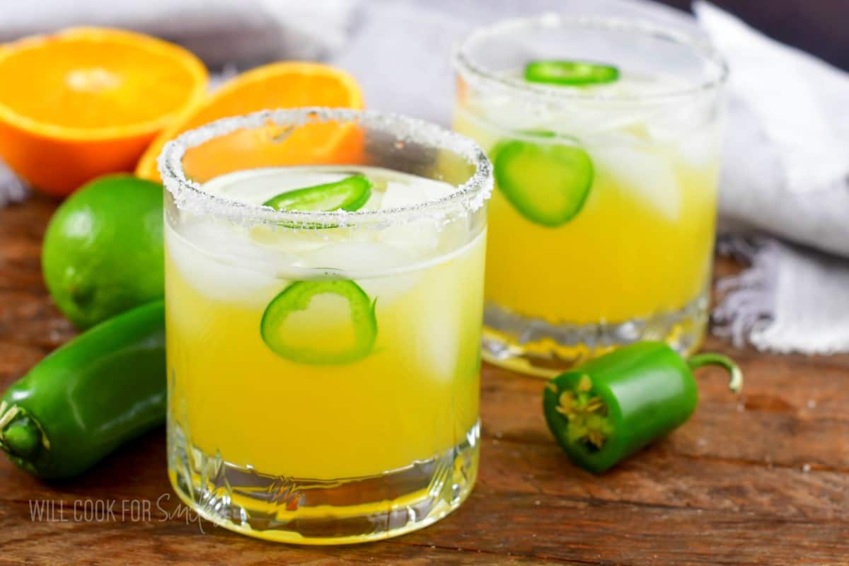 two short glasses with yellow spicy margarita with jalapeno slices.