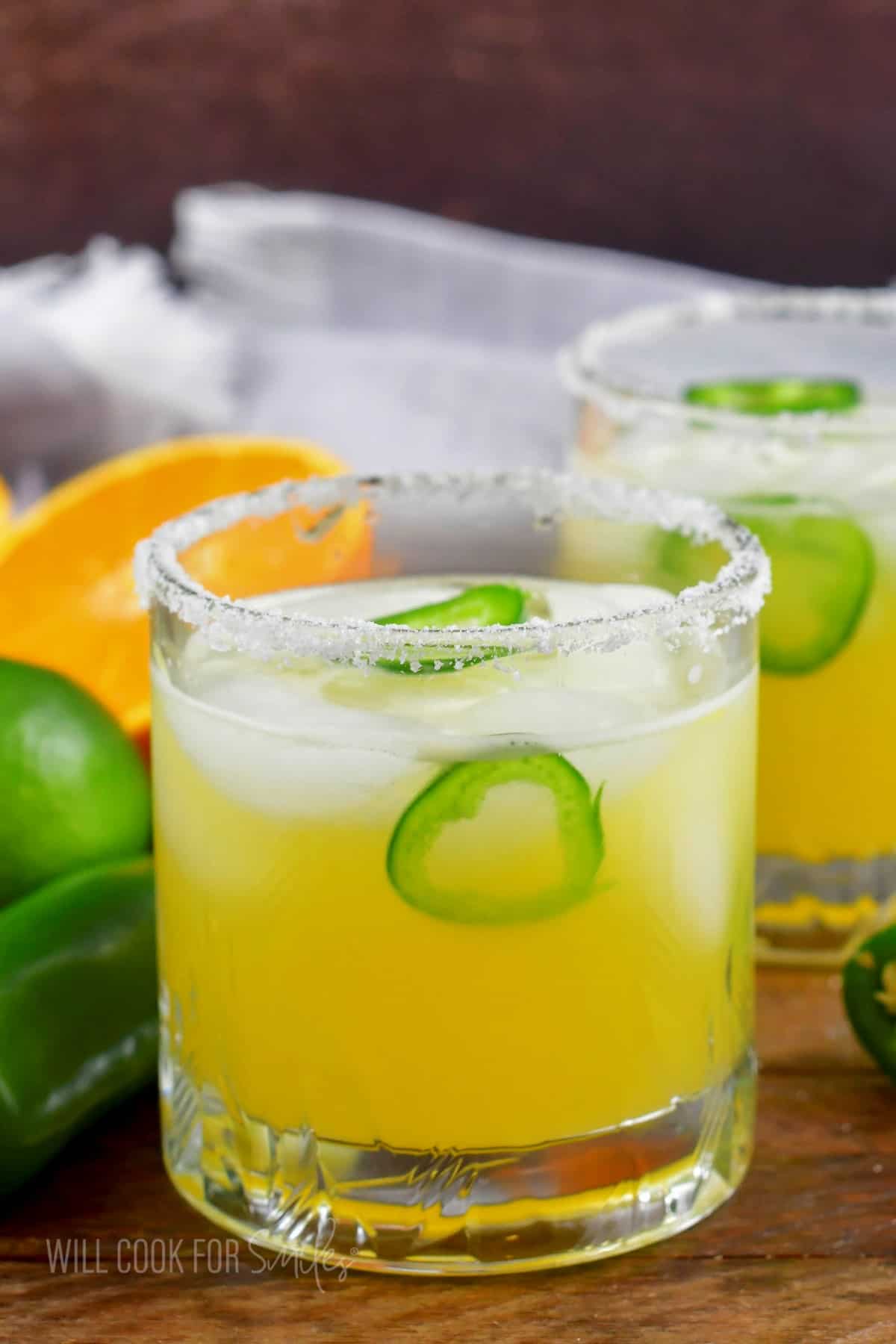 short glass with yellow spicy margarita with salted rim and jalapeno slices.