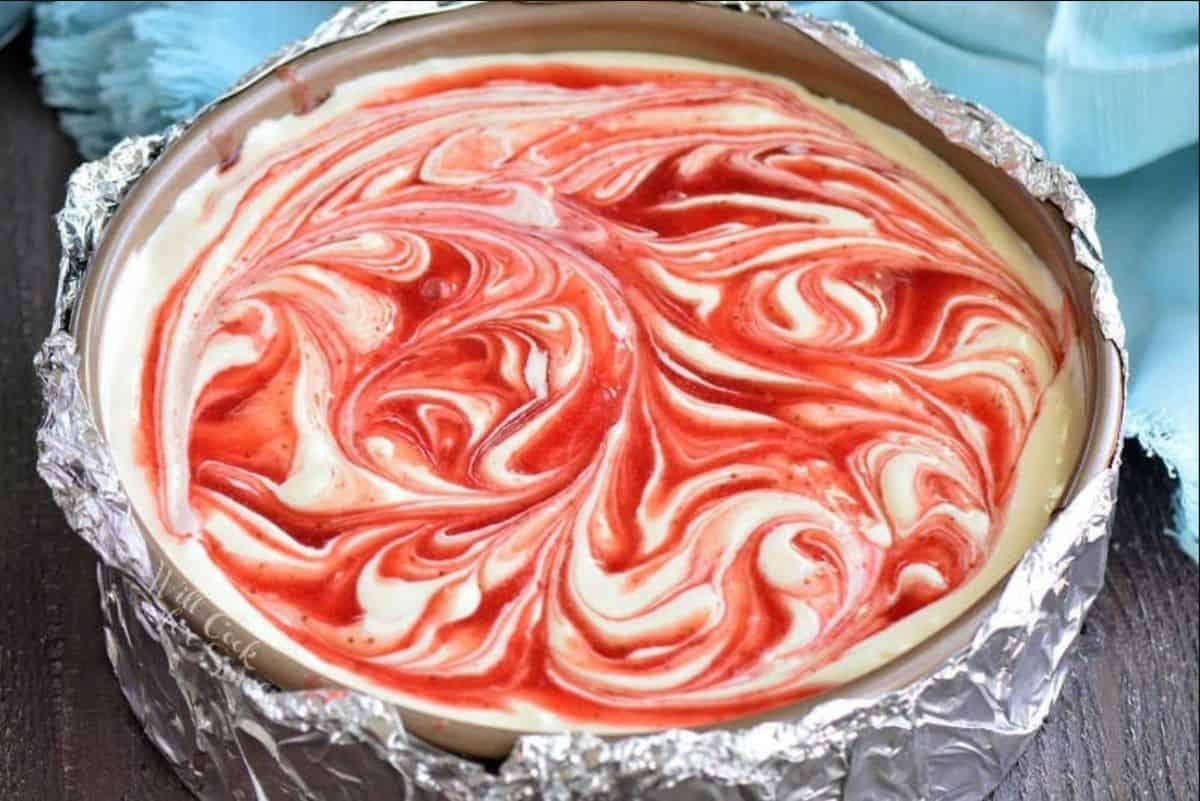 cheesecake batter in the form with strawberry sauce swirled in before baking.