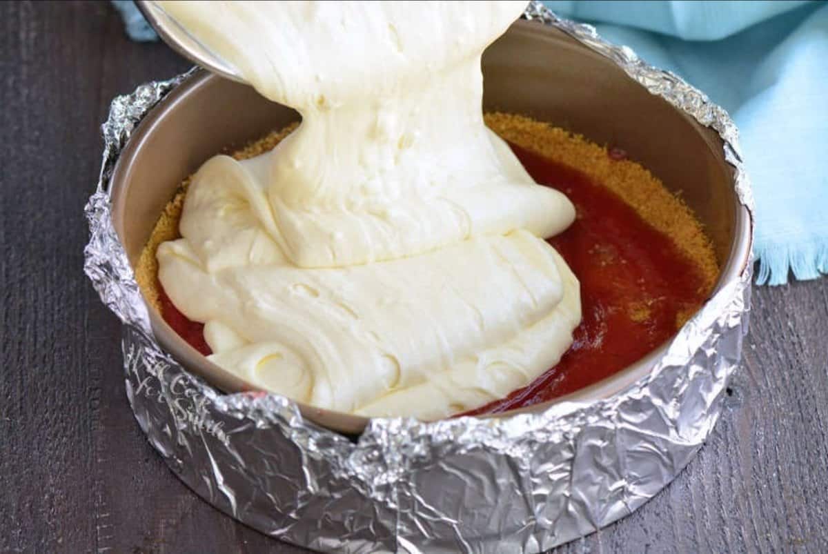 pouring cheesecake batter over the crust and strawberry sauce in the form.