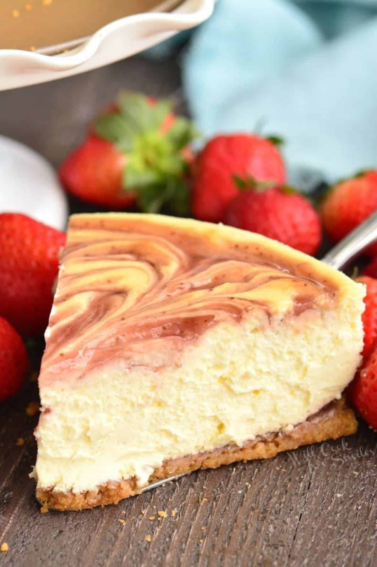 a slice of strawberry cheesecake next to cake stand with strawberries around.
