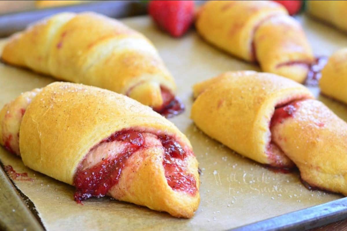 four strawberry crescent rolls on a baking sheet tray.