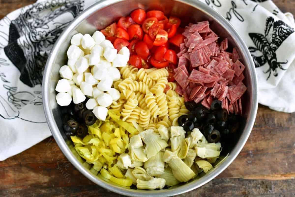 ingredients for antipasto pasta salad in metal mixing bowl before mixing.