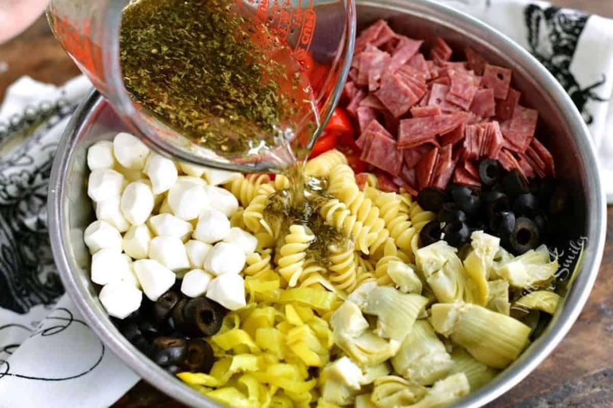 adding balsamic herb dressing to the ingredients for the pasta salad in the bowl.