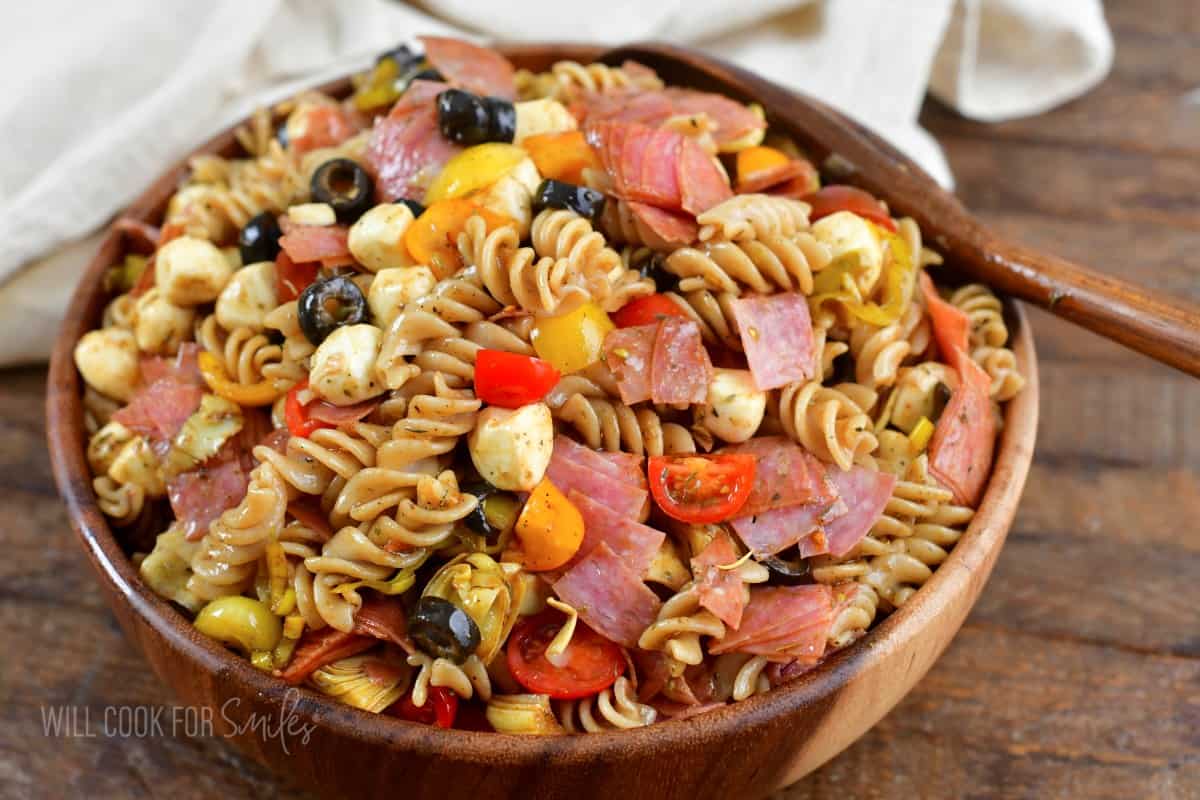 antipasto pasta salad in a wooden salad bowl with a wooden spoon.