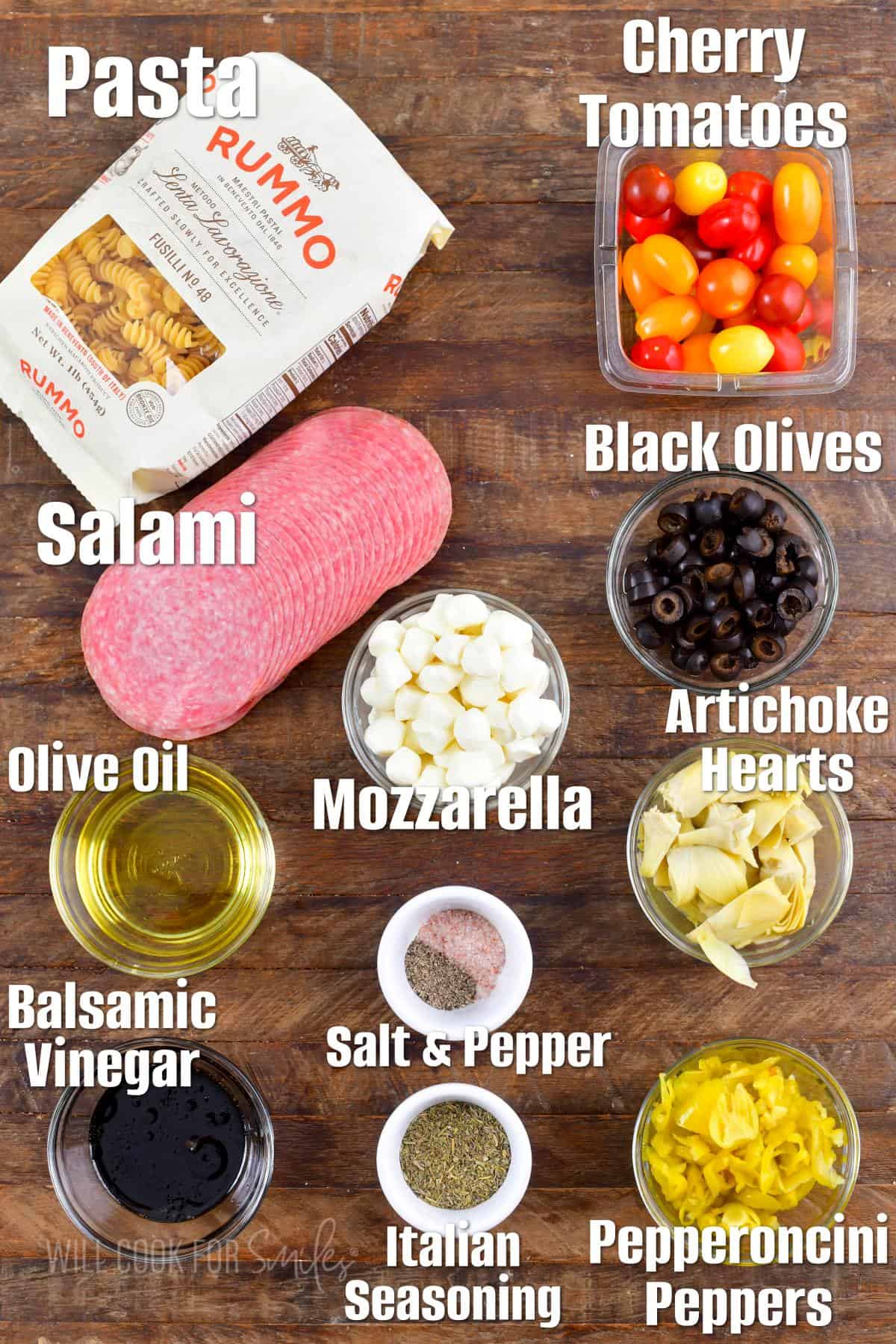 labeled ingredients for antipasto pasta salad on the wooden background.
