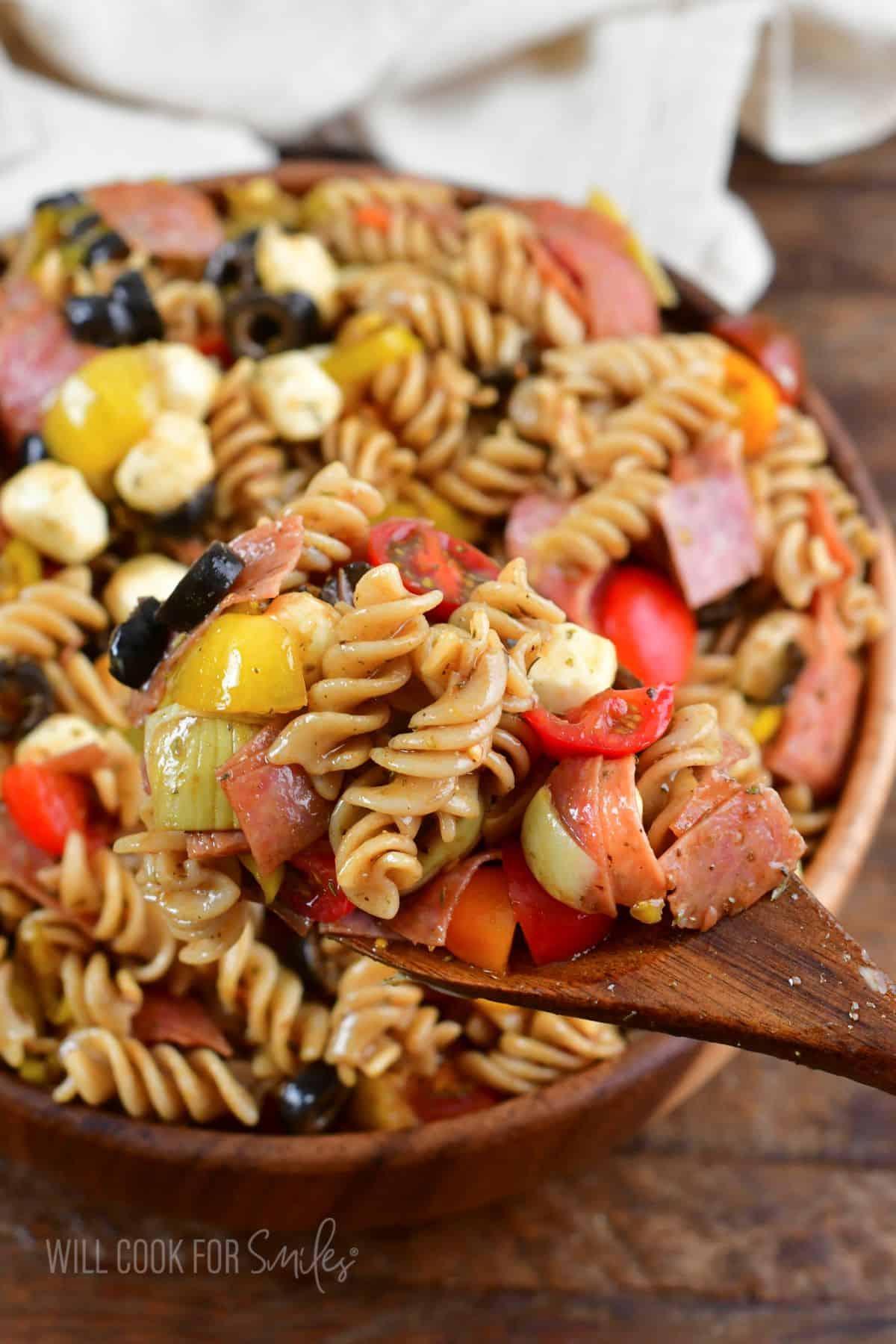 some antipasto pasta salad on the wooden spoon next to the bowl.