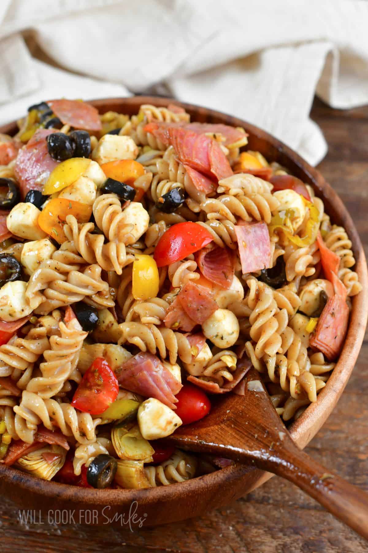 scooping out some antipasto pasta salad from a wooden bowl with a spoon.