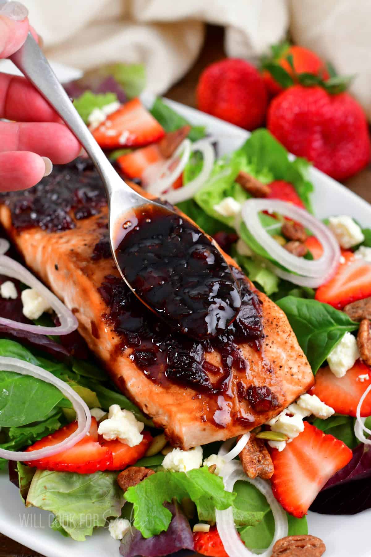 adding some balsamic glaze on top of salmon filet on a salad with strawberries and feta.