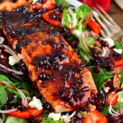 balsamic glazed salmon filet on top of a bright salad with strawberries, nuts, onion and feta.