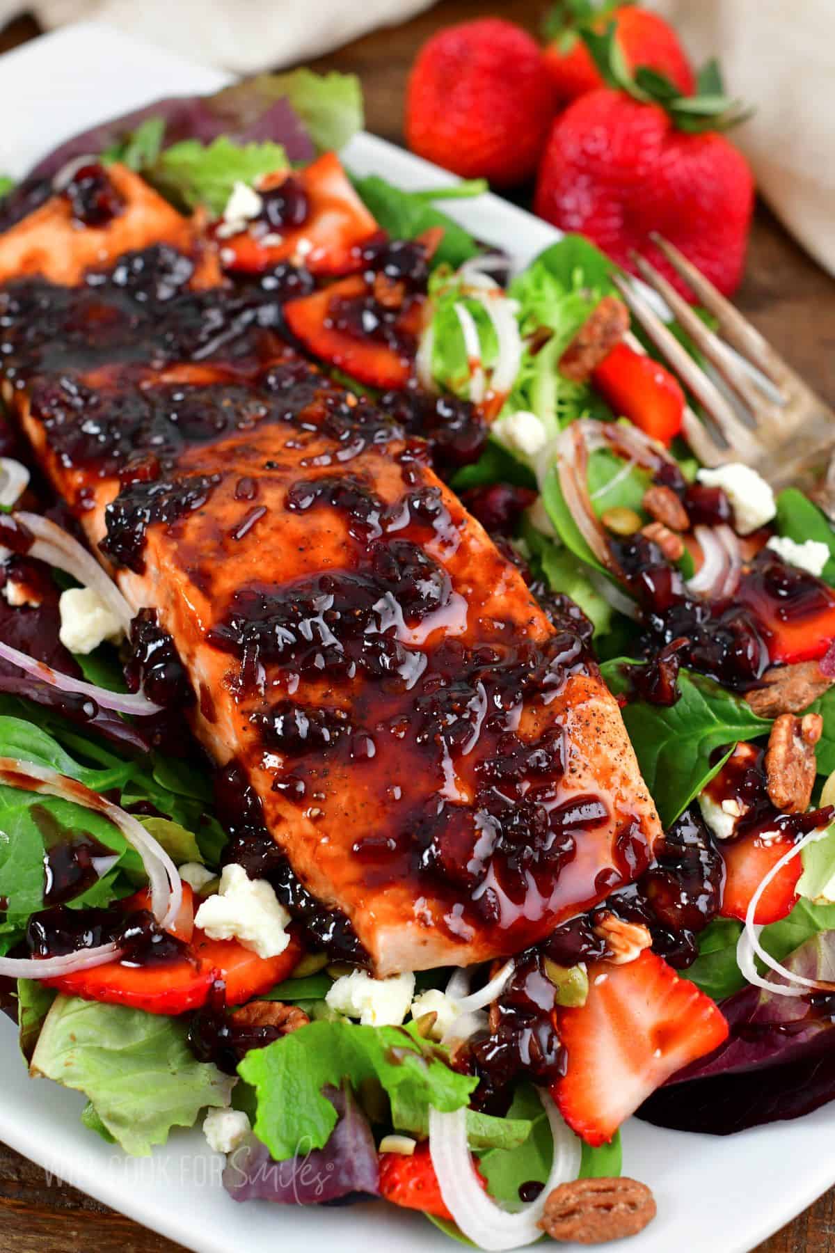 balsamic glazed salmon filet on top of a bright salad with strawberries, nuts, onion and feta.