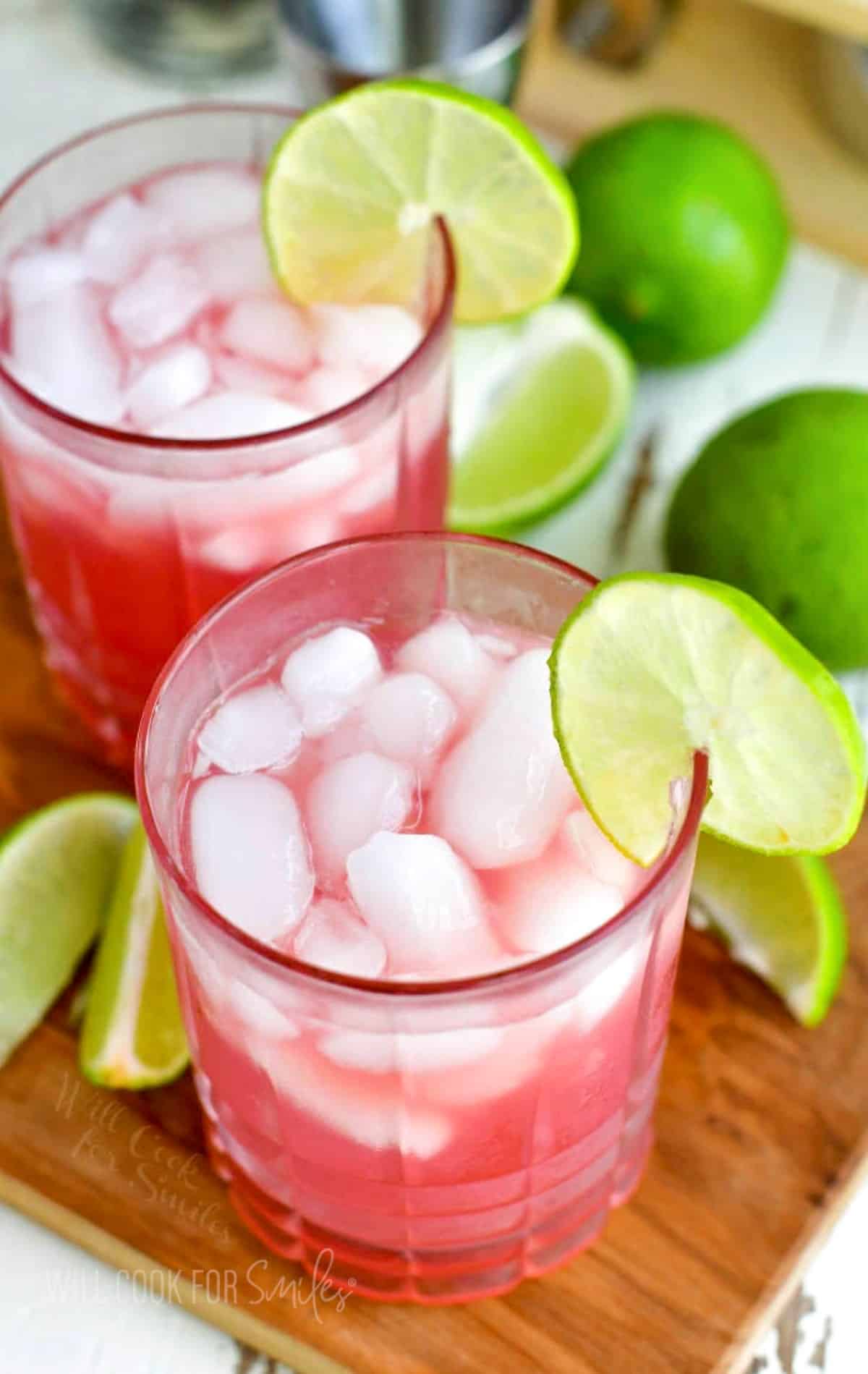 two glasses with pink cocktails ice and lime rings on the rim.