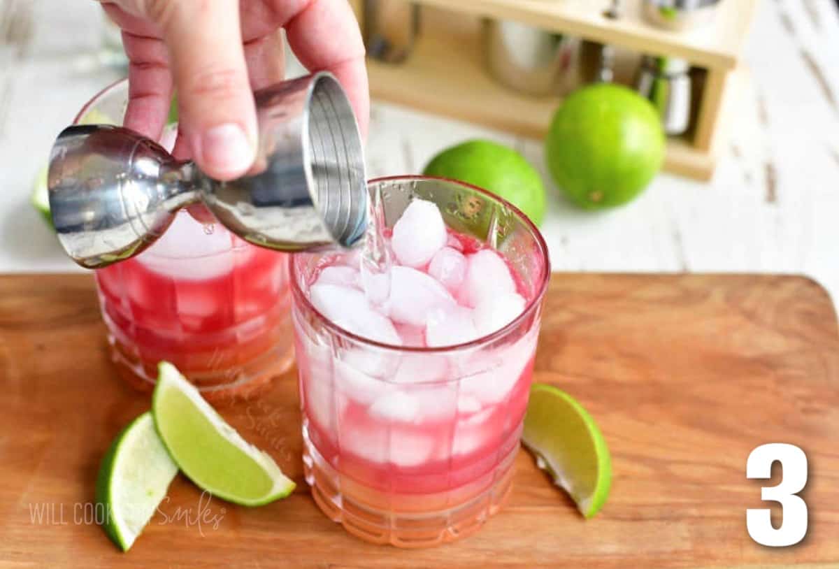 pouring in clear liquor into the glass with pink and yellow juices.