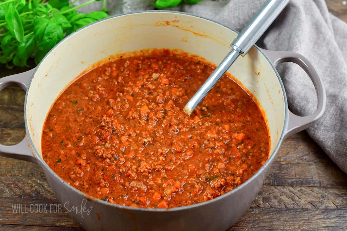 cooked red Bolognese sauce in a large pot with a ladle in it.