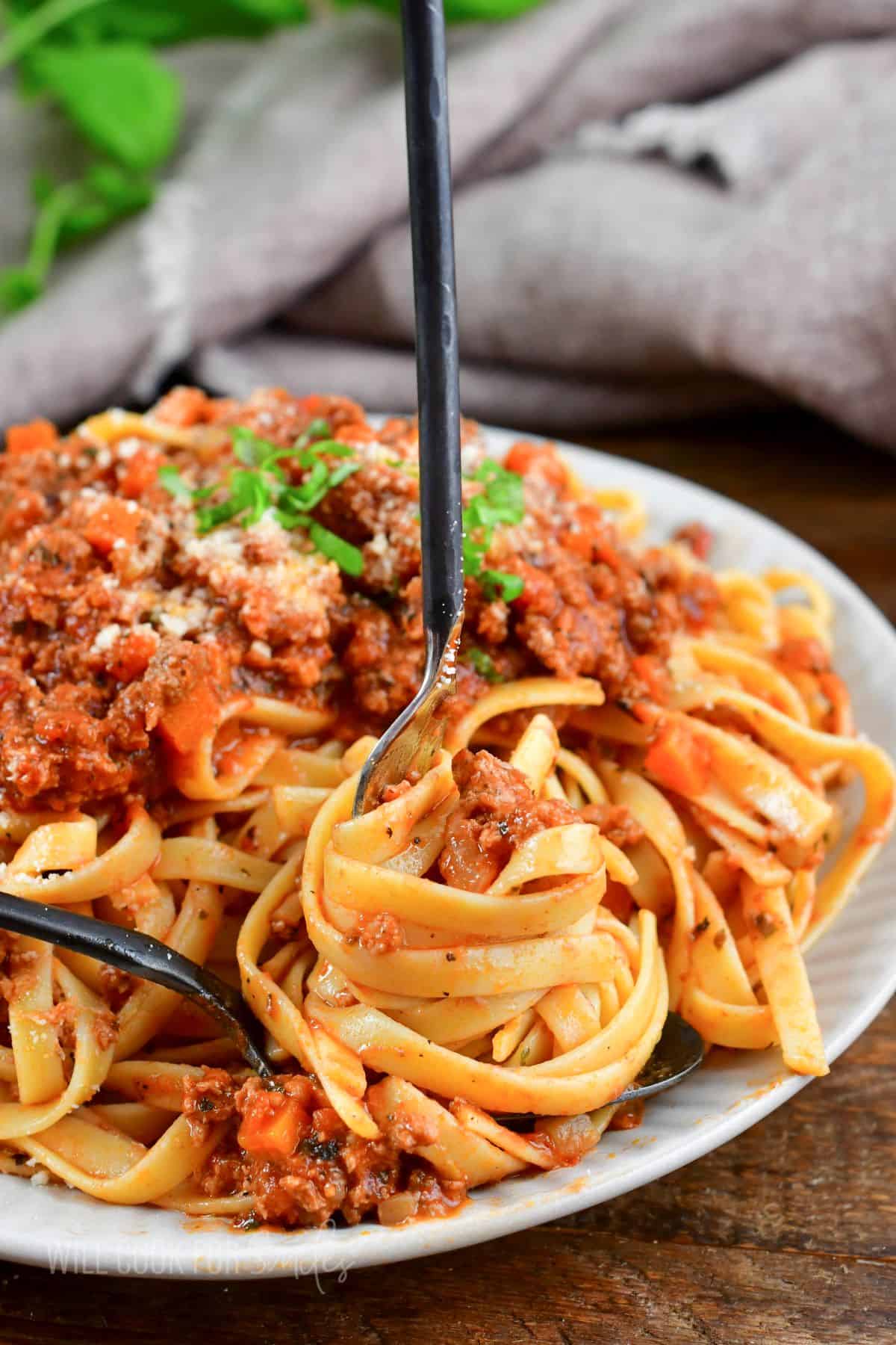 swirling some fettuccine with red meat sauce with a fork over a spoon.