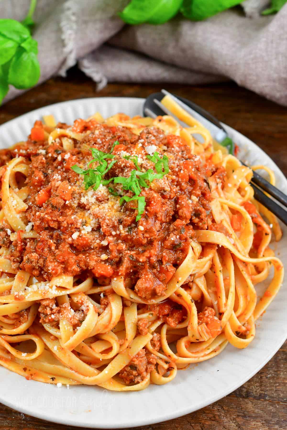 Fettuccine mixed and topped with Bolognese sauce on a plate with a fork.