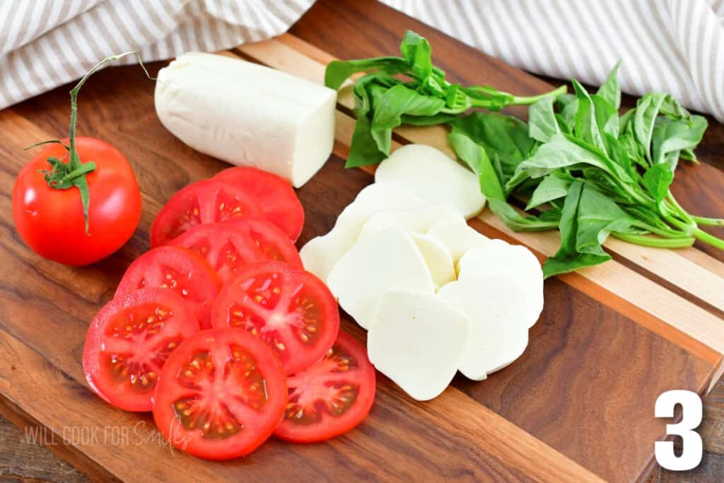 sliced tomatoes and sliced mozzarella cheese on cutting board next to basil.