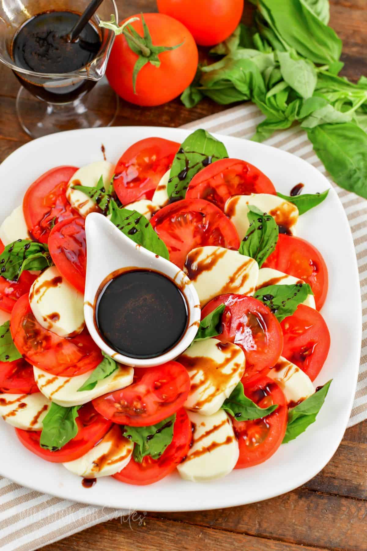 caprese salad drizzled with balsamic reduction and a cup of reduction in the middle of the plate.