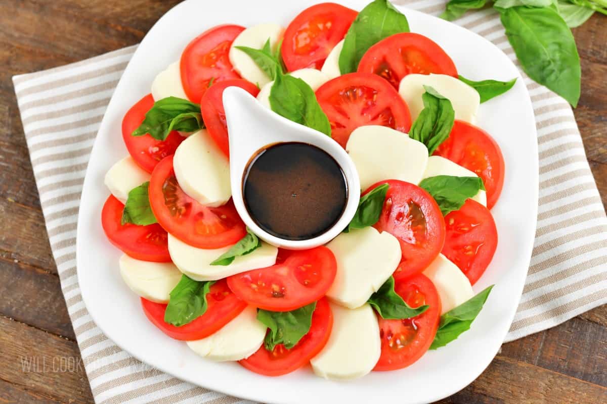 layered tomato slices, sliced mozzarella cheese, and basil leaves with some balsamic reduction in the cup.