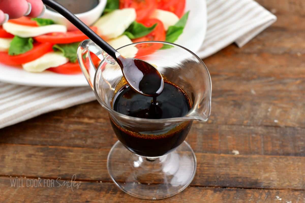 spooning out some balsamic reduction from serving cup next to caprese salad.