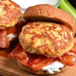 two cheddar ranch chicken burgers with bacon and sauce on a bun.