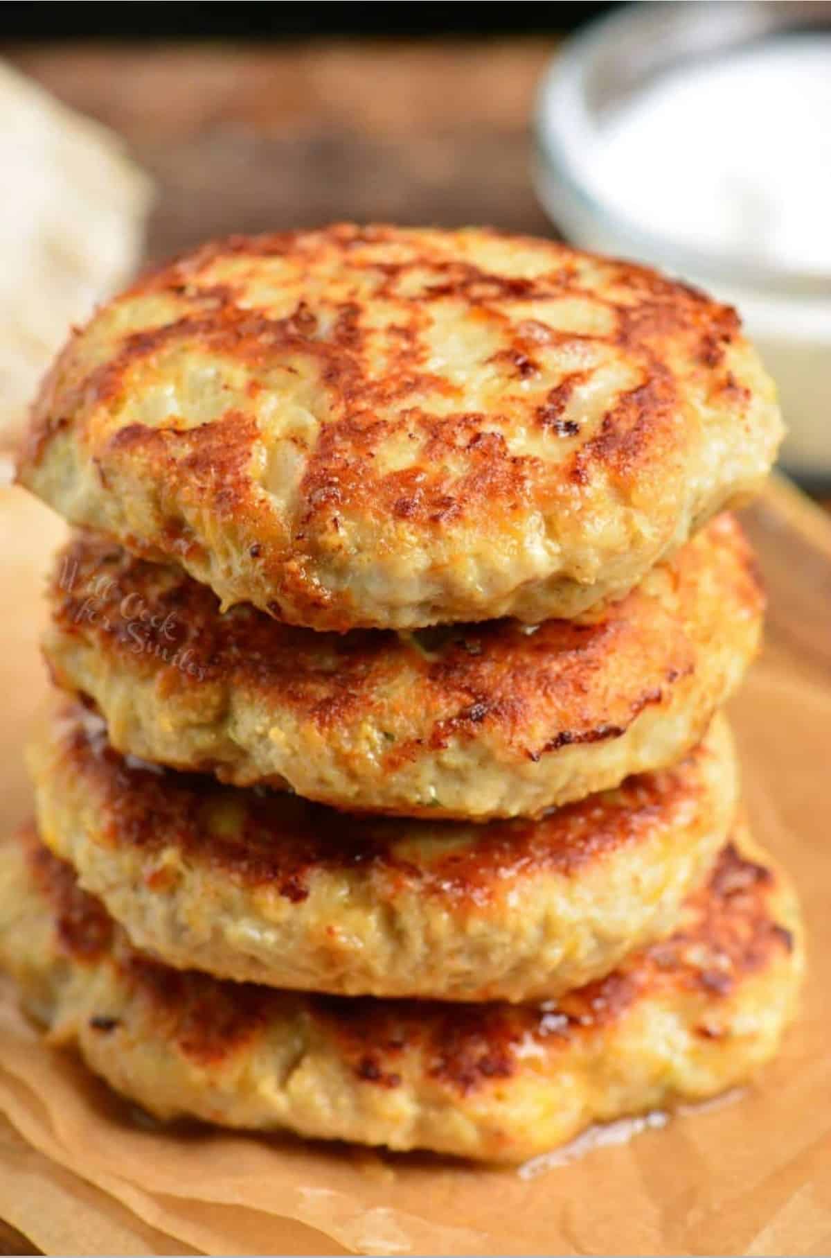 four stacked chicken burgers on parchment and ranch next to it.