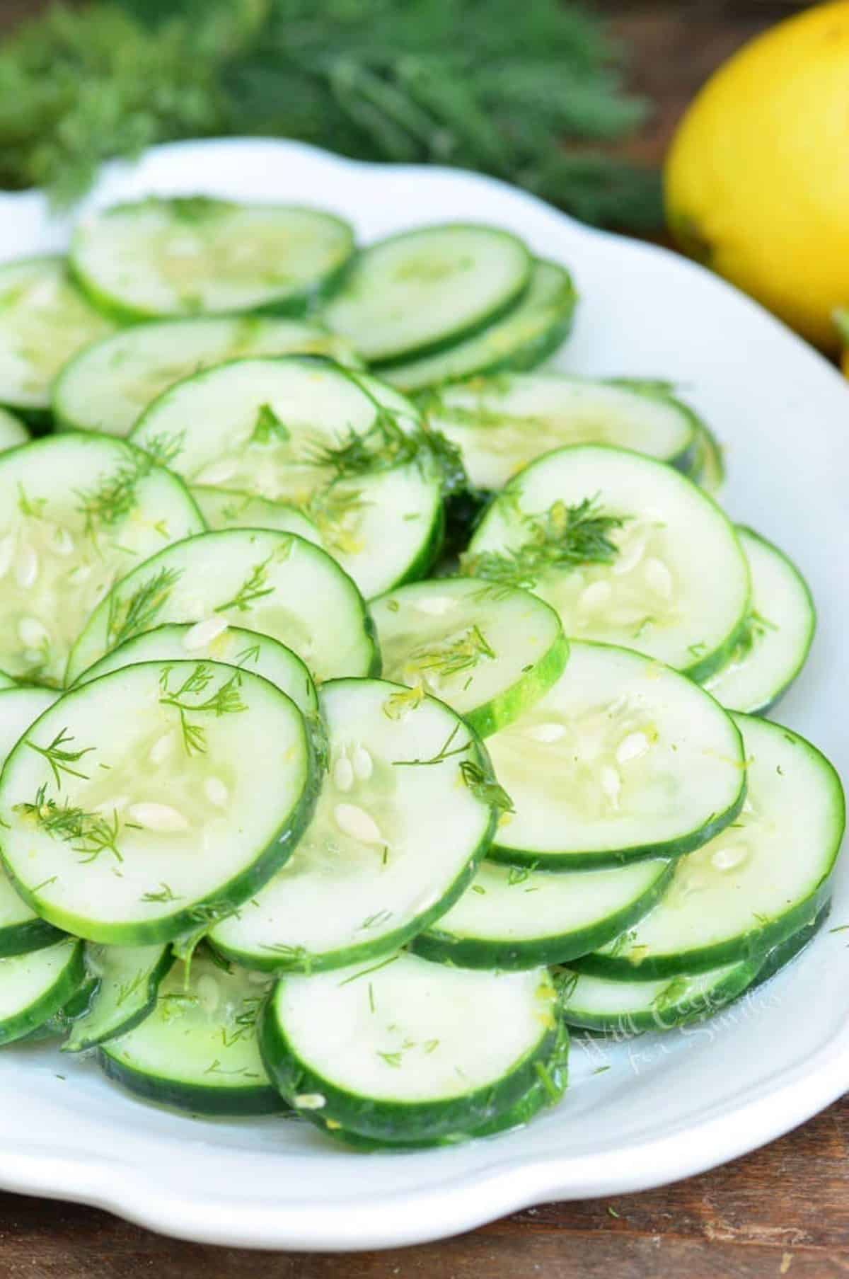 simple cucumber salad in a plate nest to dill and lemons.