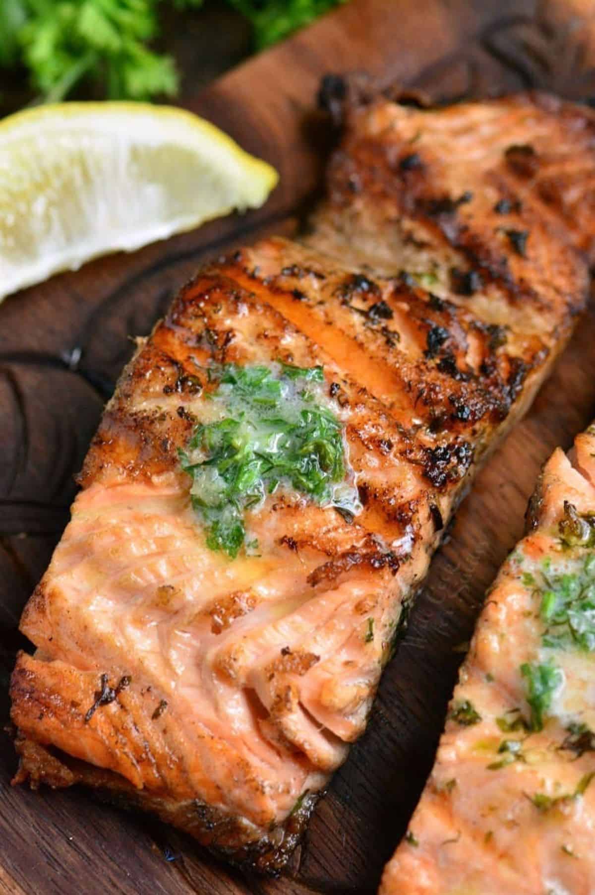 a grilled salmon filet topped with melting herb butter and lemon wedge.